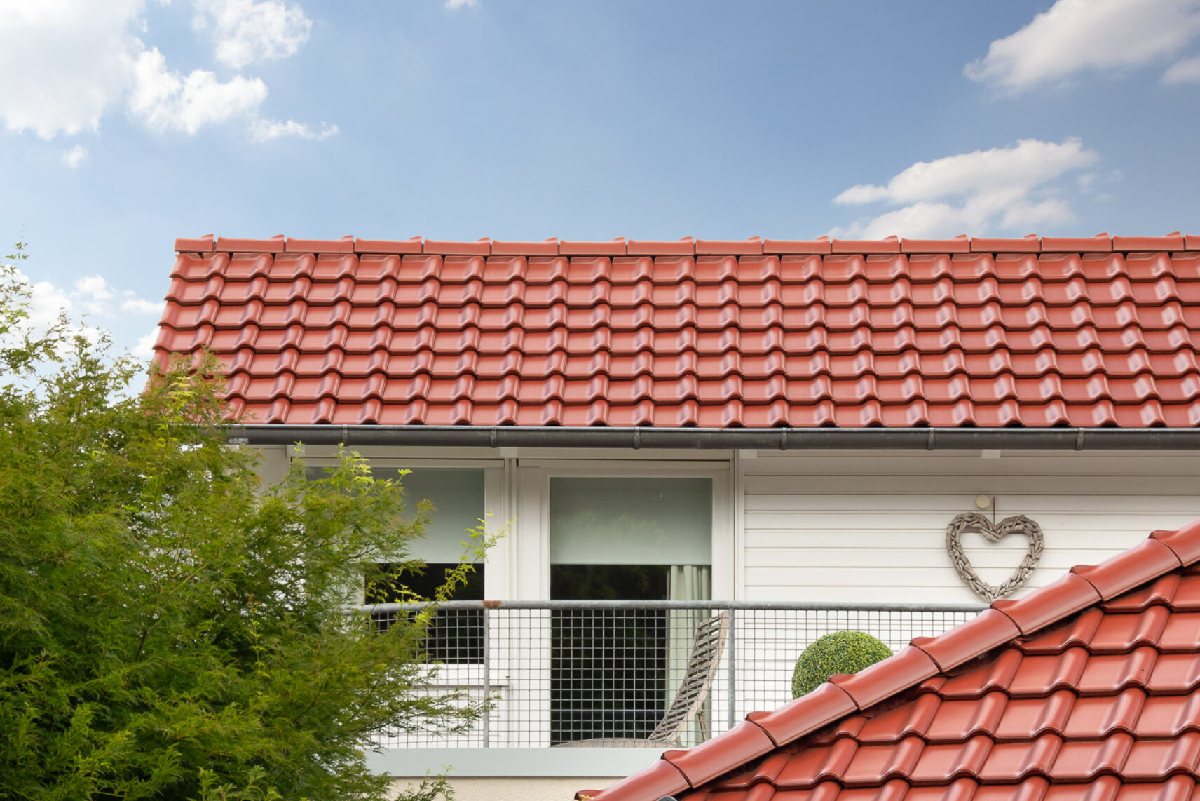 Detached house with pitched roof and J11v roof tile in matt Tuscan red. The focus of the image is on the ridge and roof covering