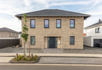 ront view of a detached house with beige clinker bricks and hipped roof covered with J13v flat roof tiles in matt slate grey