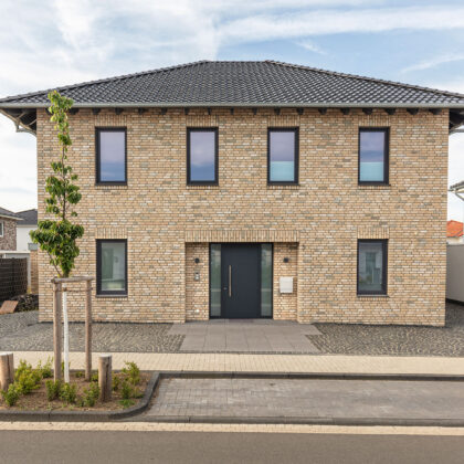 ront view of a detached house with beige clinker bricks and hipped roof covered with J13v flat roof tiles in matt slate grey