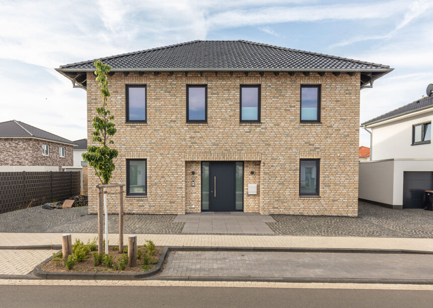 ront view of a detached house with beige clinker bricks and hipped roof covered with J13v flat roof tiles in matt slate grey